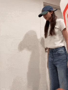 a woman wearing a white shirt and blue jeans is standing in front of a door