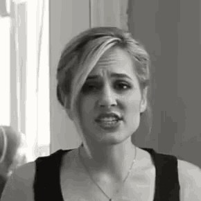 a woman is wearing a black tank top and a necklace and making a funny face .