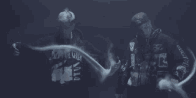 two men are standing next to each other in a dark room with smoke coming out of their mouths