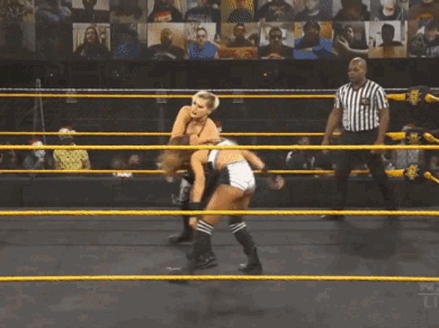 two women are wrestling in a ring with a referee and a crowd watching