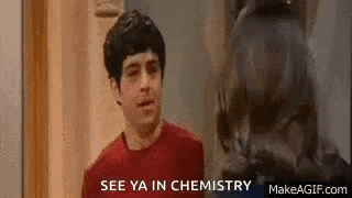 a man in a red shirt is standing in front of a door and talking about chemistry .