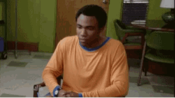 a man in an orange shirt is sitting in a chair looking at his watch