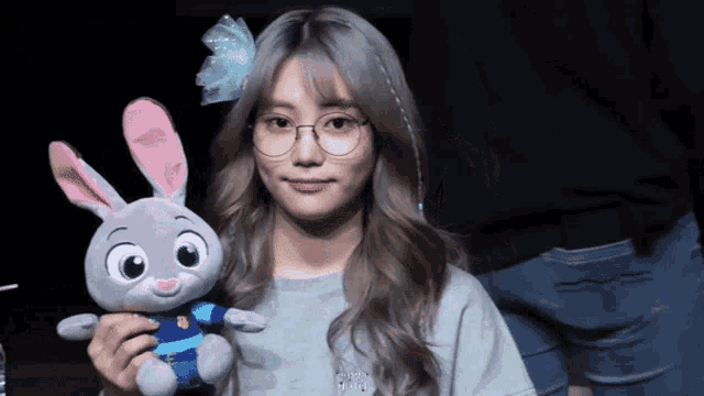 a woman wearing glasses holds a stuffed bunny