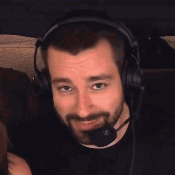 a man with a beard is wearing headphones and a microphone and smiling .