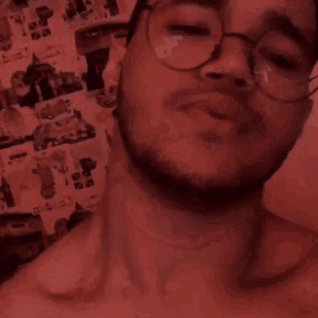 a man with glasses and a beard is taking a selfie in front of a red background .