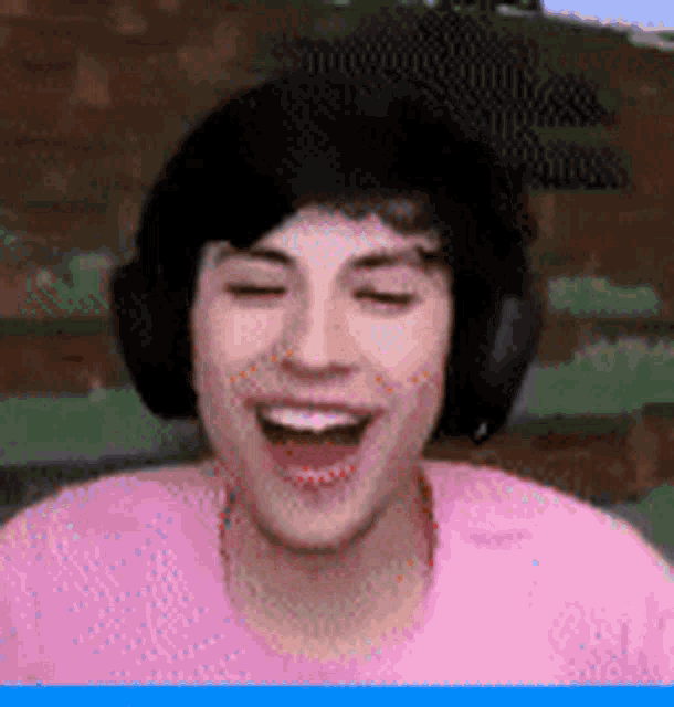 a young man wearing headphones and a pink shirt is laughing with his mouth open .