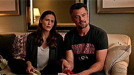 a man and woman are sitting on a couch and the man is wearing a georgia shirt