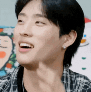 a young man wearing a plaid shirt and earrings smiles