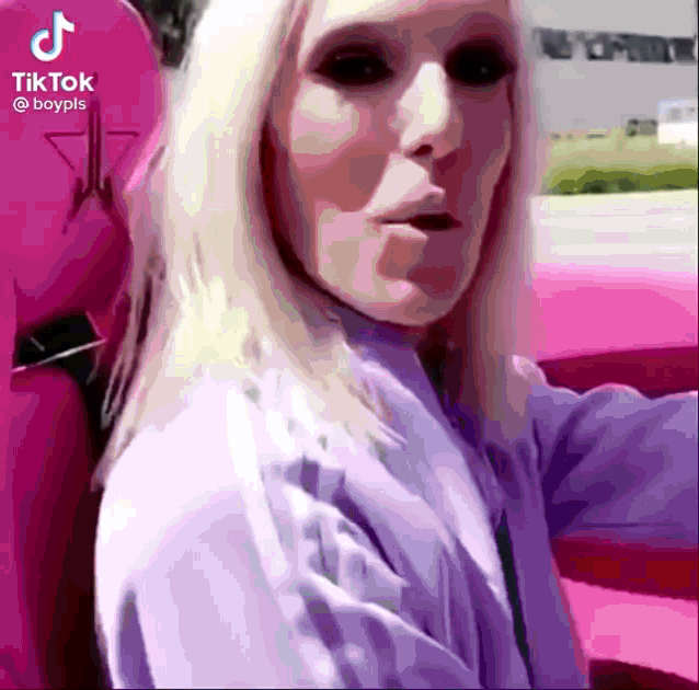 a woman with black eyes is sitting in a pink car with a tiktok logo in the background .