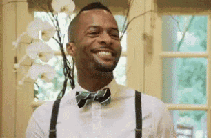 a man wearing a bow tie and suspenders is smiling while standing in front of a window .