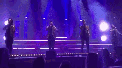 a group of men are standing on a stage holding microphones and dancing .