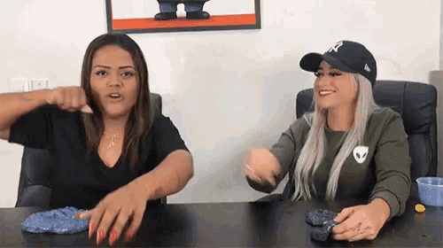 two women are playing with slime at a table .