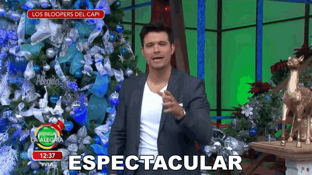 a man in a suit stands in front of a christmas tree and a sign that says spectacular