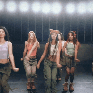 a group of young women are dancing on a stage in front of a row of lights