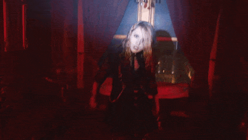 a woman is dancing in a dark room with a red curtain behind her