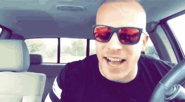 a man wearing sunglasses is driving a car and smiling