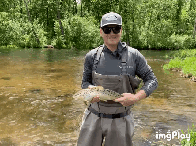 a man wearing a shirt that says sky life is holding a brown trout