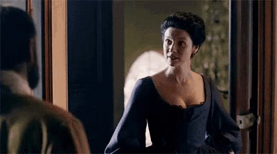 a woman in a blue dress is standing next to a man in a room and talking to him .