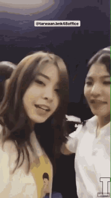 two girls are standing next to each other and one of them is wearing a yellow shirt with a picture of a man on it .