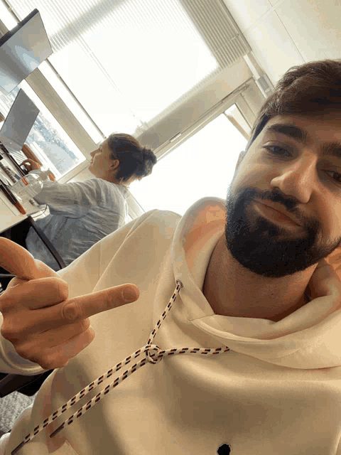 a man with a beard wearing a white hoodie is giving the middle finger