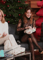 two women are sitting in front of a christmas tree