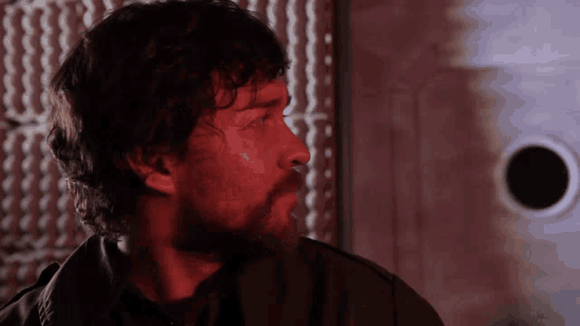 a man with a beard looks to the side in a dark room