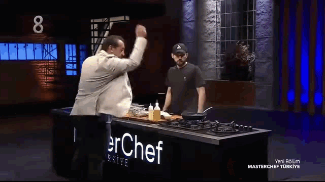 a man in a suit is cooking in a pan on a stove while another man watches .