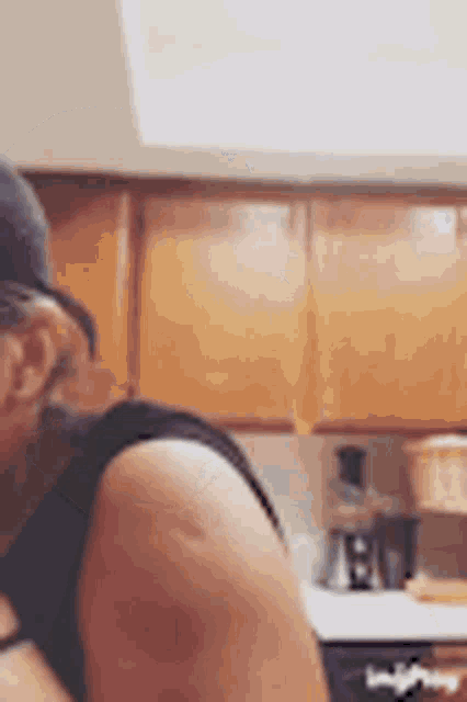 a woman is standing in a kitchen wearing a hat and glasses .