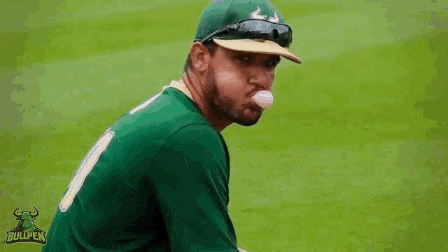 a baseball player blowing a bubble with a bullpen logo behind him