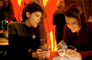 two women are sitting at a table looking at a cell phone