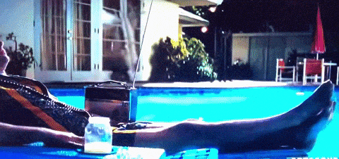 a man is laying in a swimming pool with a radio and a cup of milk