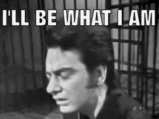 a black and white photo of a man in a jail cell with the words `` i 'll be what i am '' .