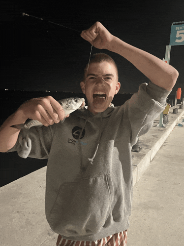 a boy wearing a hoodie that says snow goose on it holds a fish