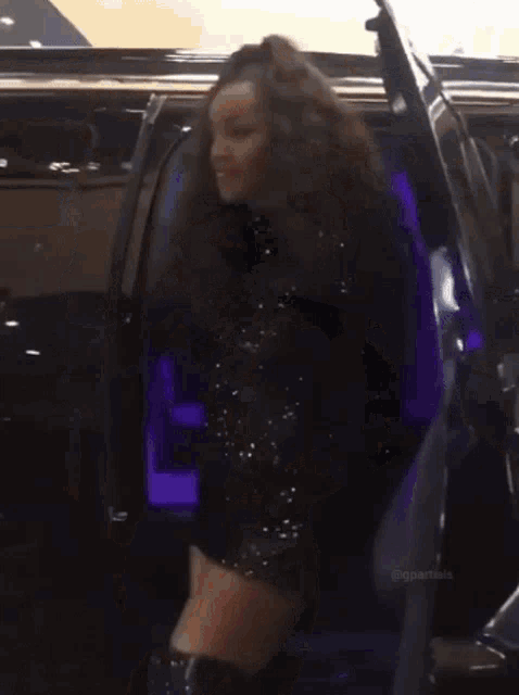 a woman with curly hair is standing next to a car with a wheel on it