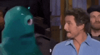a man in a blue shirt is standing next to a green stuffed animal and talking to it .