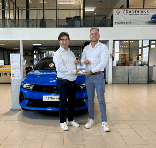 two men standing in front of a blue astra hybrid car