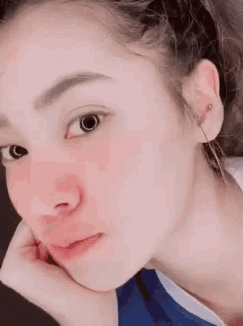 a close up of a woman 's face with her hand on her chin and earrings .