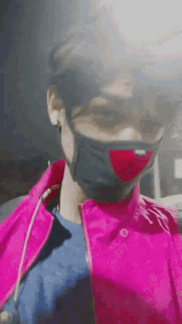 a person wearing a pink jacket and a black mask with a red heart on it