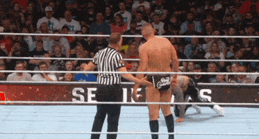 a referee stands between two wrestlers in a wrestling ring with a crowd watching