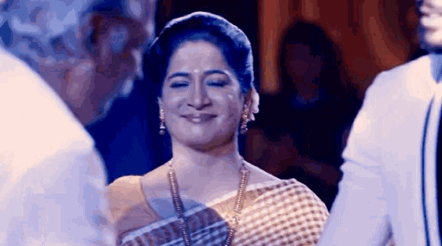 a woman in a saree is smiling while standing next to a man in a white suit .