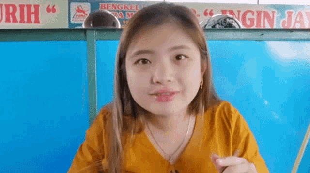 a woman in a yellow shirt is sitting at a table in front of a sign that says ' a ' on it .