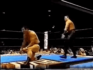 a wrestler kicking another wrestler in a wrestling ring with a crowd watching