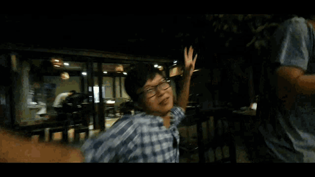 a man in a plaid shirt and glasses is dancing in a dark room