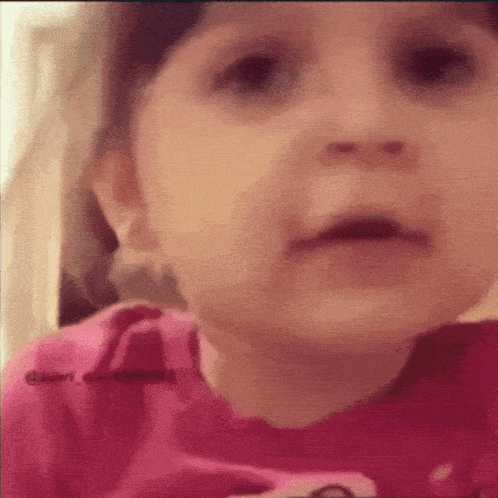 a baby in a pink shirt is making a face