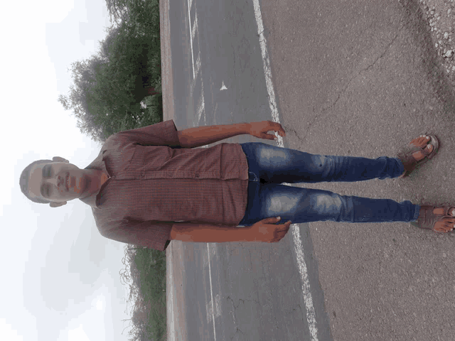 a man in a plaid shirt and blue jeans is standing on the side of the road