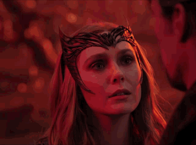 a woman with a crown on her head looks at a man in a dark room