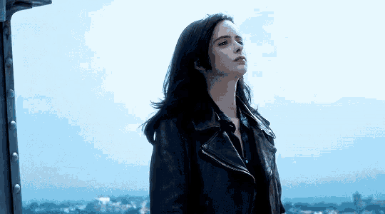 a woman in a black leather jacket stands on a rooftop overlooking a city