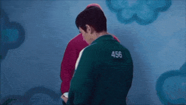 a man in a green jacket with the number 456 on it is standing next to a man in a red jacket .