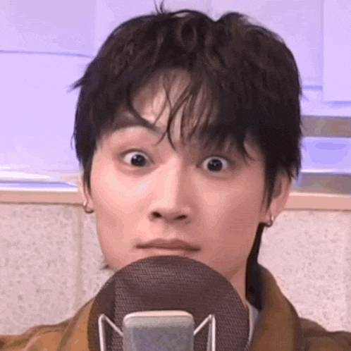 a young man is making a funny face while holding a microphone in front of his face .