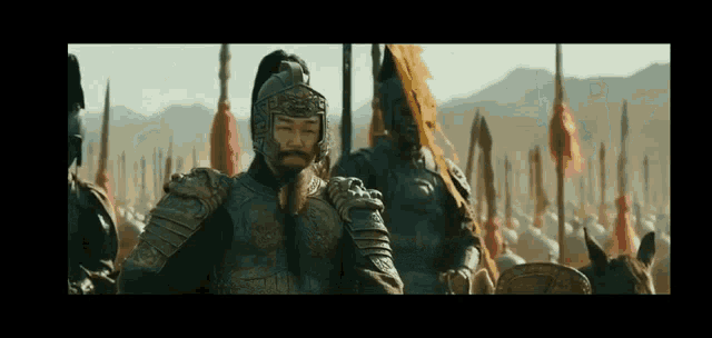 a man in armor is standing in front of a large army of soldiers on horseback .